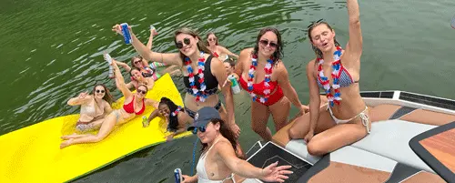 Group of women celebrating on a boat and floating mat while enjoying water sports on Percy Priest Lake in Nashville.